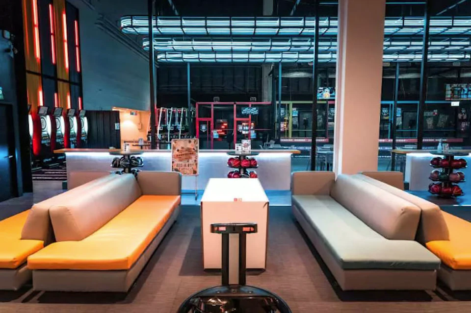 A lounge area with two sofas facing each other and a white table between them, in front of a modern bar with neon lights.