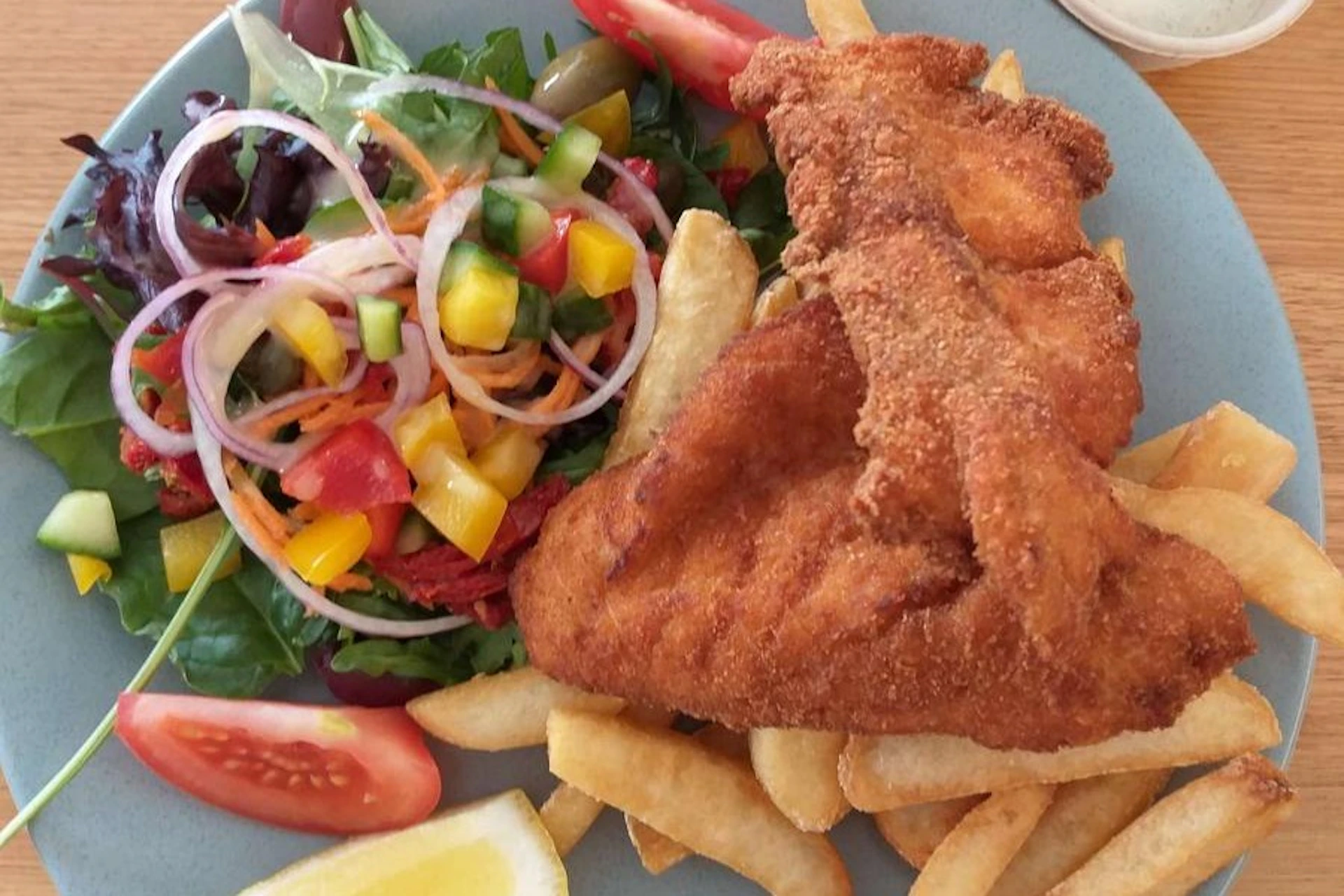 Crispy fried fish served with golden fries, a fresh mixed salad, and a lemon wedge on a plate.