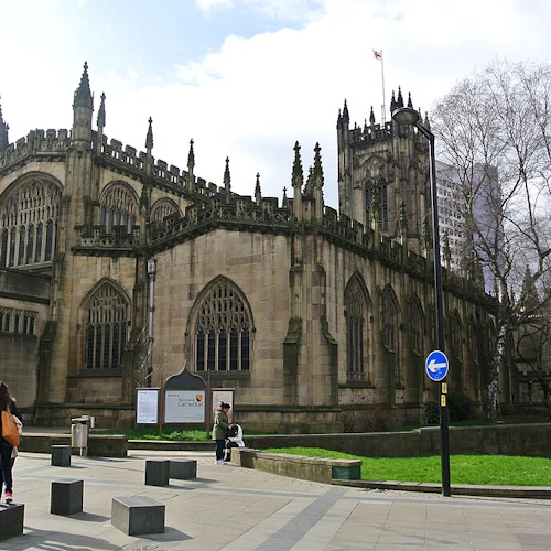 Katedral i gotisk stil med stora välvda fönster, ett torn och spiror. Tre fotgängare och en gräsyta i närheten.