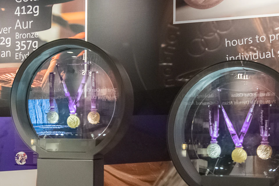 Museum exhibit featuring circular glass displays with medals, informational posters, images, and objects on a wall behind.