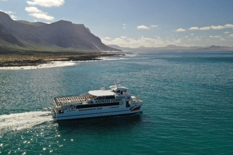 一艘名为“Express Ferry”的渡轮在多岩石的海岸线附近航行，在晴朗的天空下有着连绵起伏的山丘，云层分散。