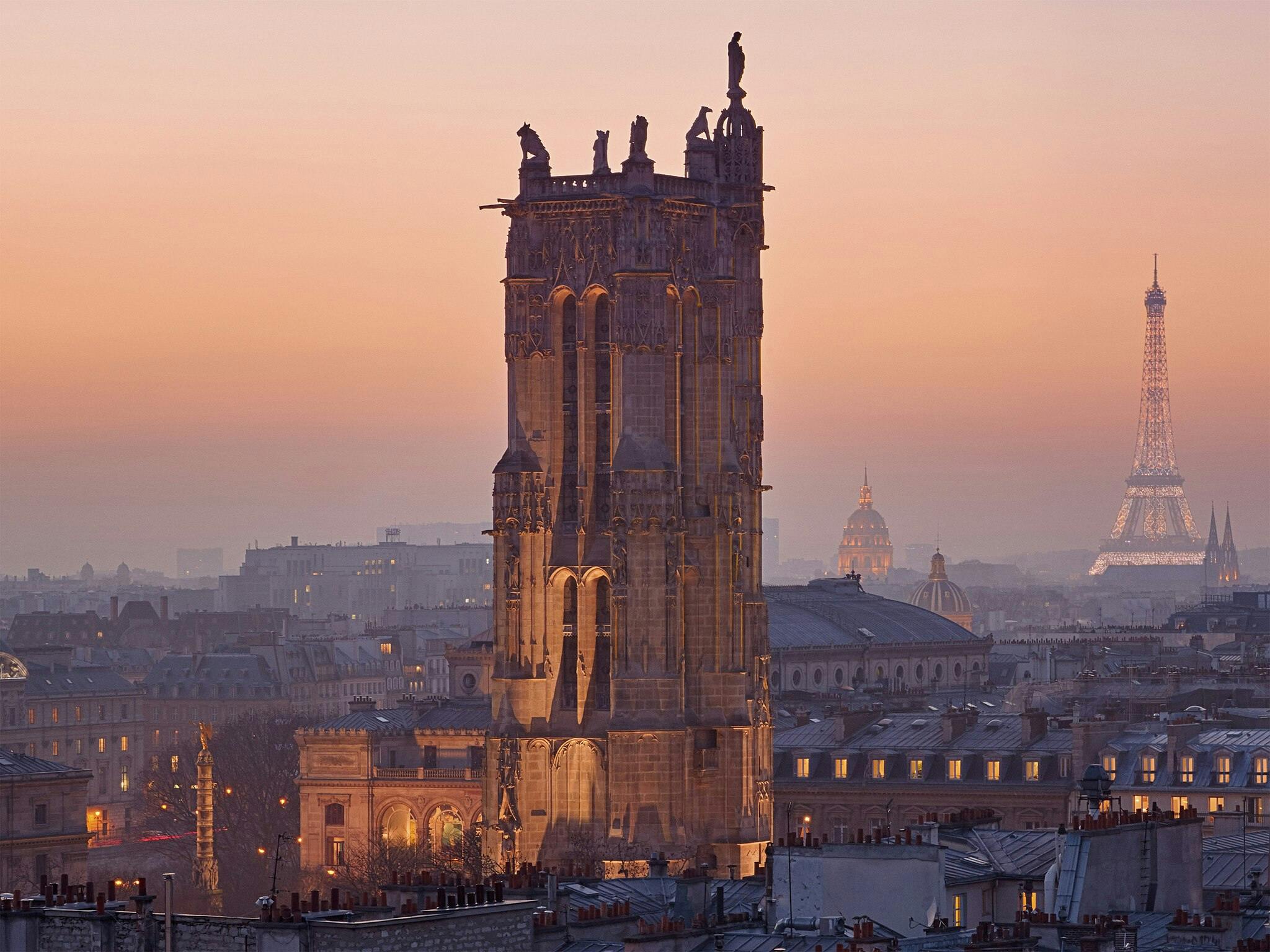 Gothic tower in Paris with prominent sculptures at dusk, Eiffel Tower and cityscape in the hazy background.