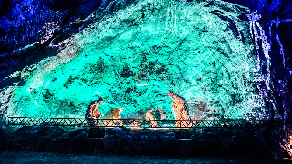 A illuminated nativity scene with statues of Mary, Joseph, baby Jesus, and animals against a textured, green-lit cave wall.
