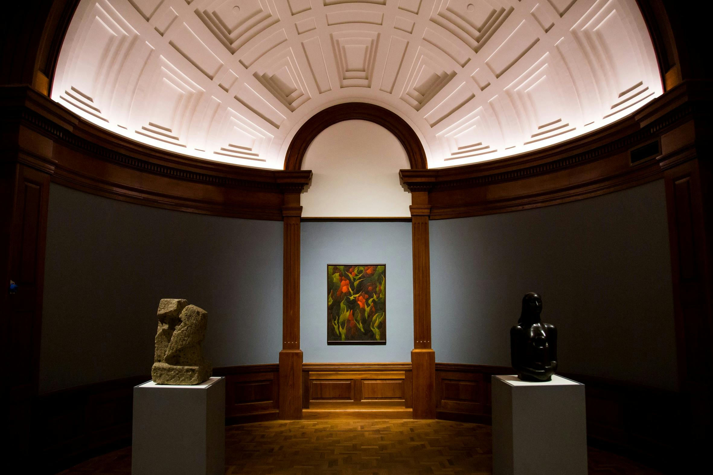 A museum gallery displaying a colorful painting between two abstract sculptures on pedestals under a domed ceiling.
