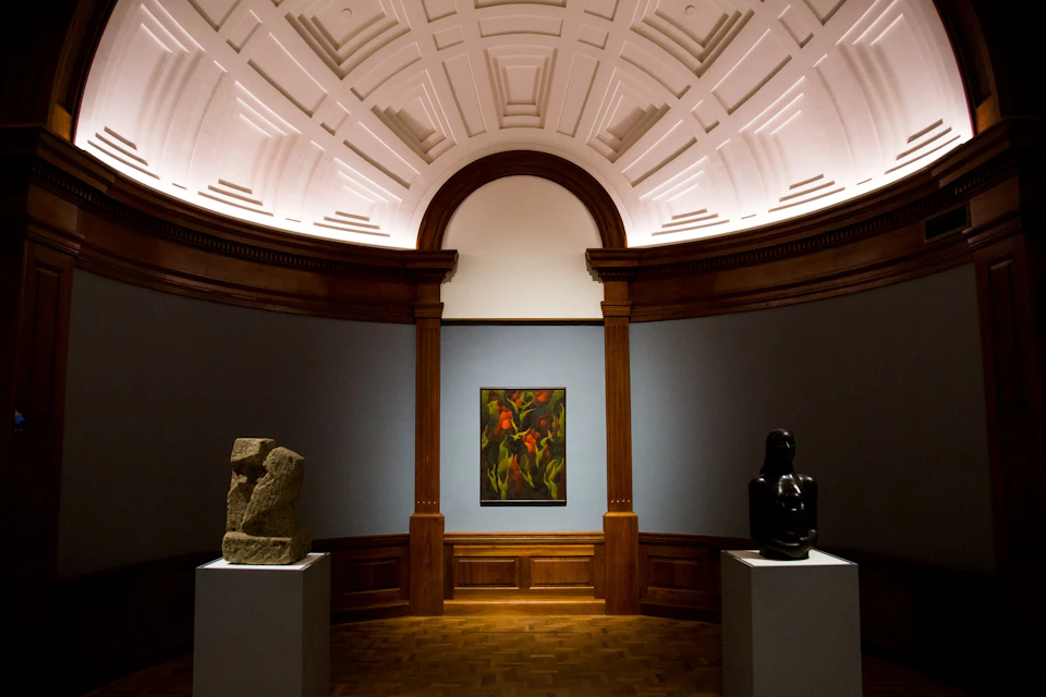 A museum gallery displaying a colorful painting between two abstract sculptures on pedestals under a domed ceiling.