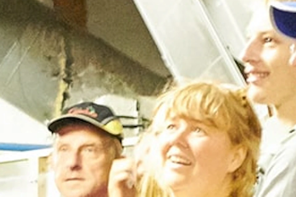 A tour guide gestures while speaking to an attentive group inside a museum with display cases and an overhead ventilation system.