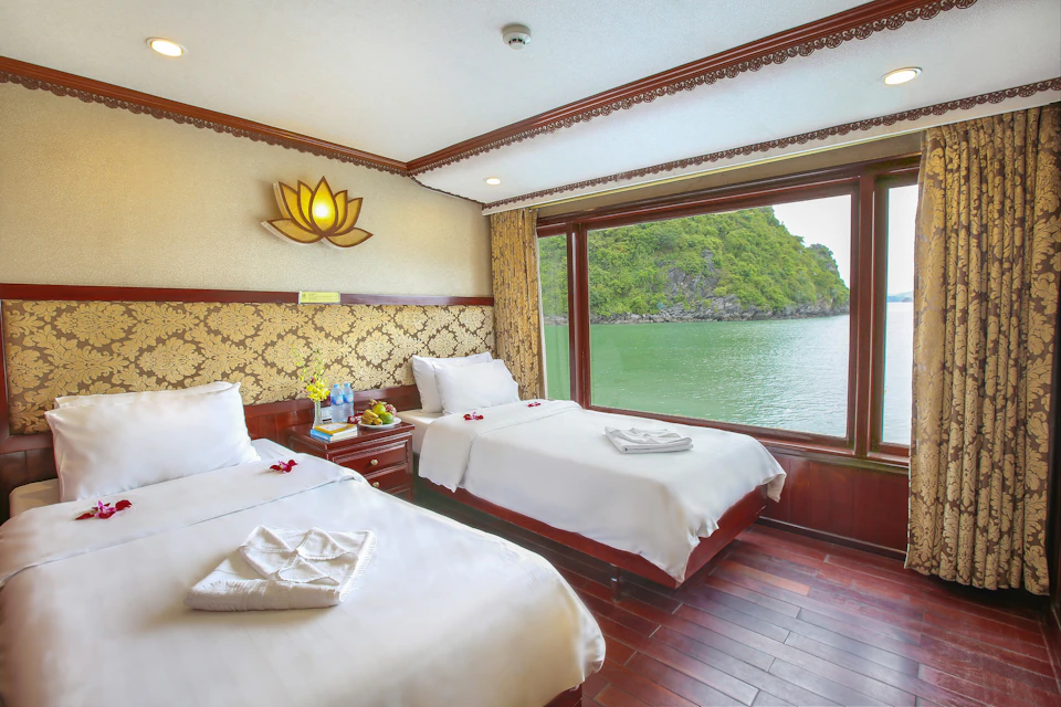 Hotel room with two twin beds, large window overlooking a serene lake and green hills, and elegant decor.