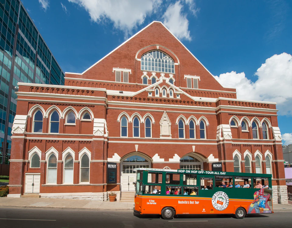 A red-brick building with arched windows and a green-and-orange tourist bus parked in front.