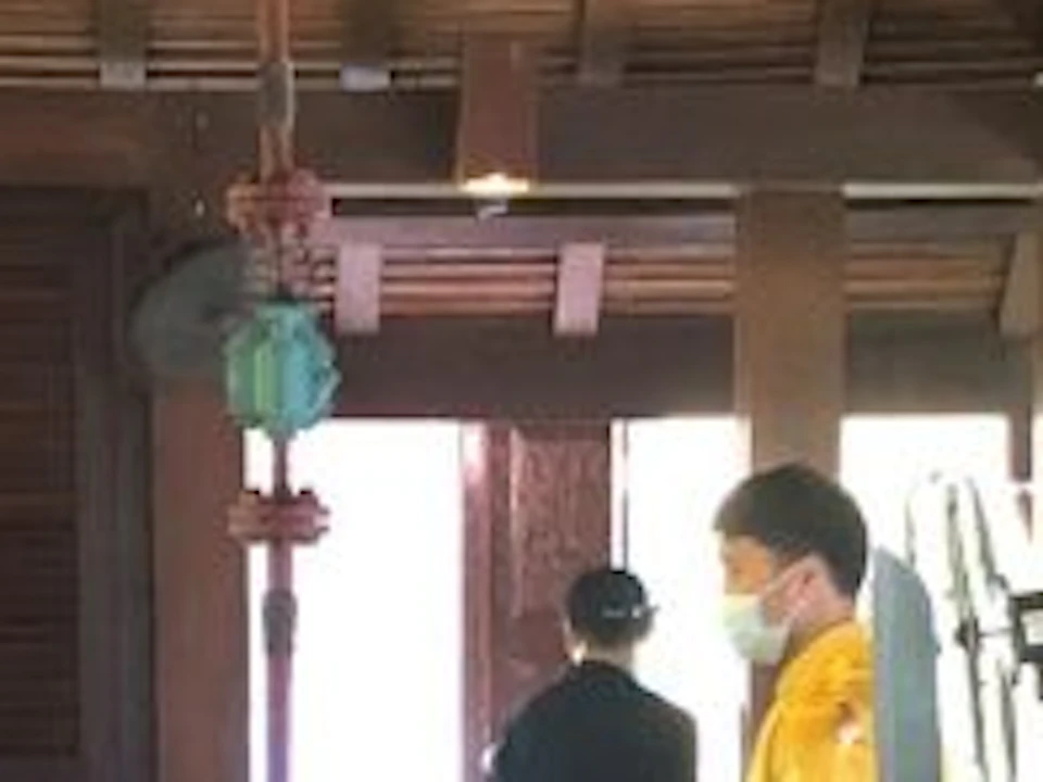 Three people in a rustic kitchen, wearing aprons, cooking at individual stations under a high, wooden ceiling with hanging lights.