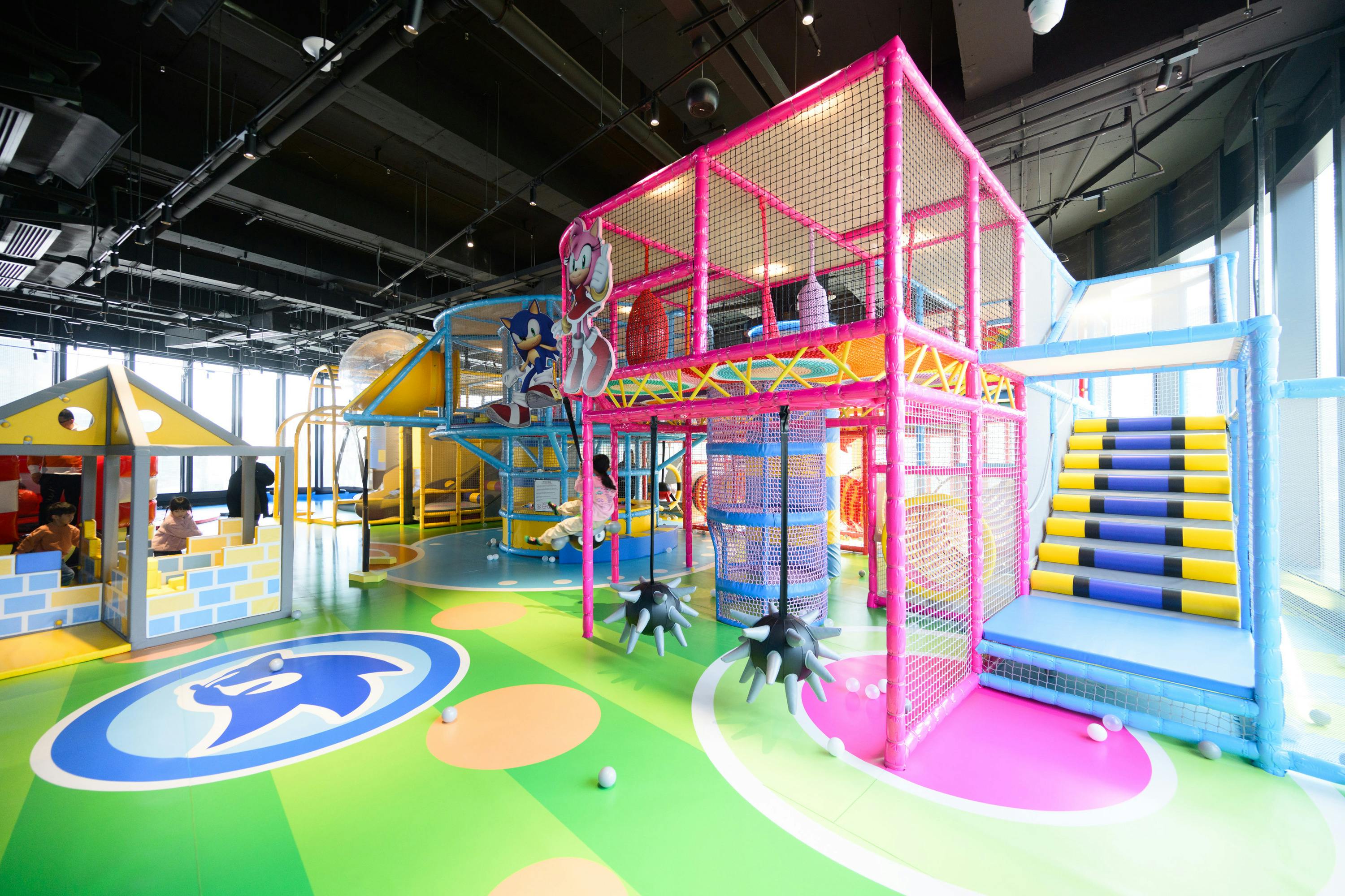 Indoor colorful playground with structures, slides, and cartoon-themed decorations, featuring vibrant flooring.