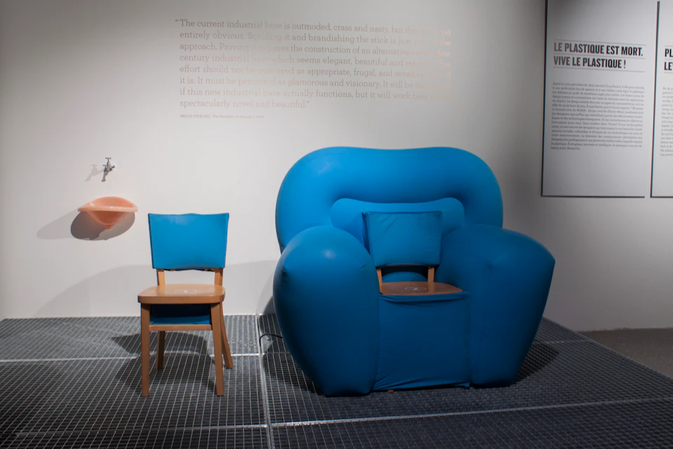 Two chairs: a small blue wooden chair and a larger, blue padded armchair, against a wall with faint text.