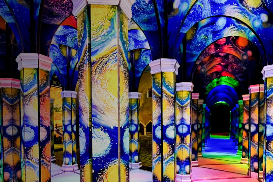 A hallway with columns and arches illuminated by colorful projections resembling Van Gogh's Starry Night painting.