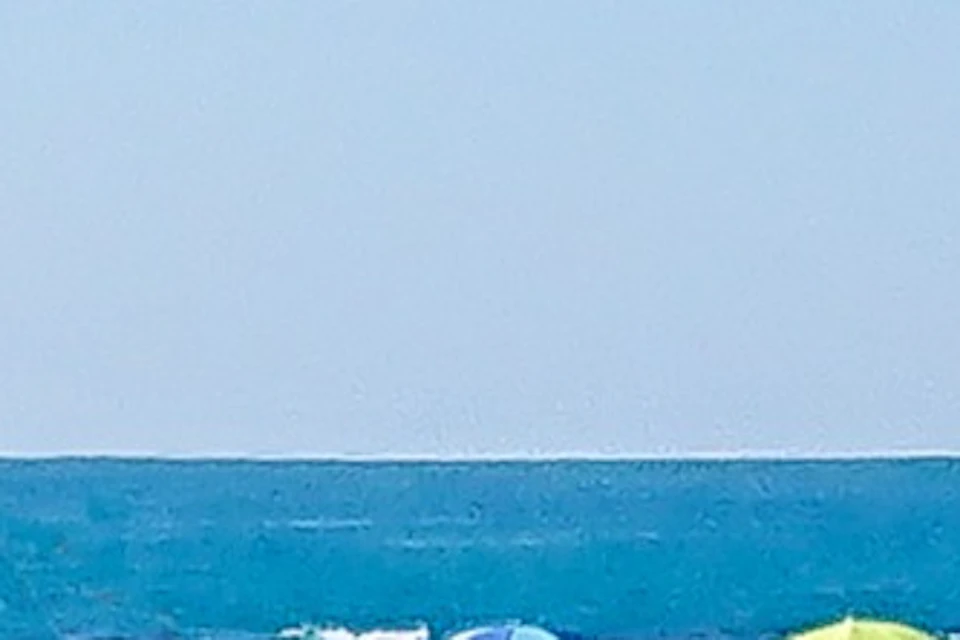 Three people riding bicycles on a coastal road beside the beach under a clear blue sky.
