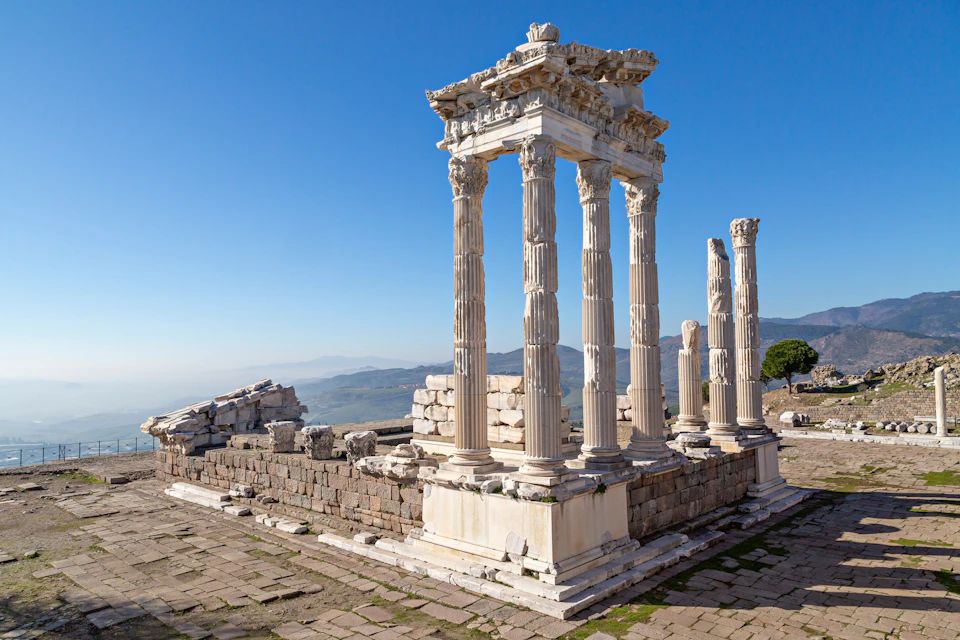 Ancient ruins with tall, white stone columns and partially standing structures under a clear blue sky.