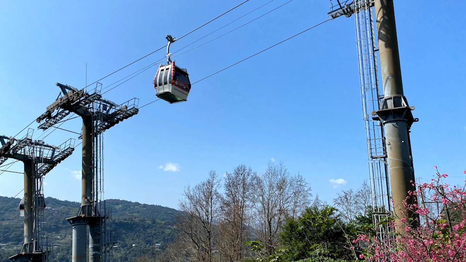 A cable car suspended on wires over a natural landscape with trees and a clear blue sky.