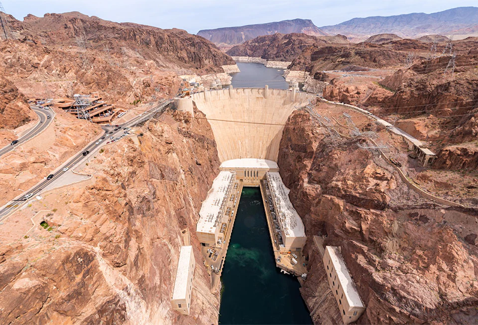 Aerial view of the Hoover Dam holding back a large reservoir, surrounded by rocky terrain, with buildings and roads visible nearby.