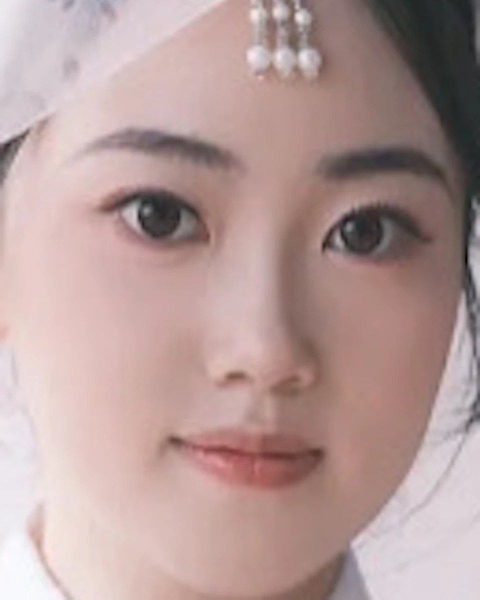 A woman wearing a traditional outfit with a light pink floral pattern and white top, adjusting a sheer veil on her head.