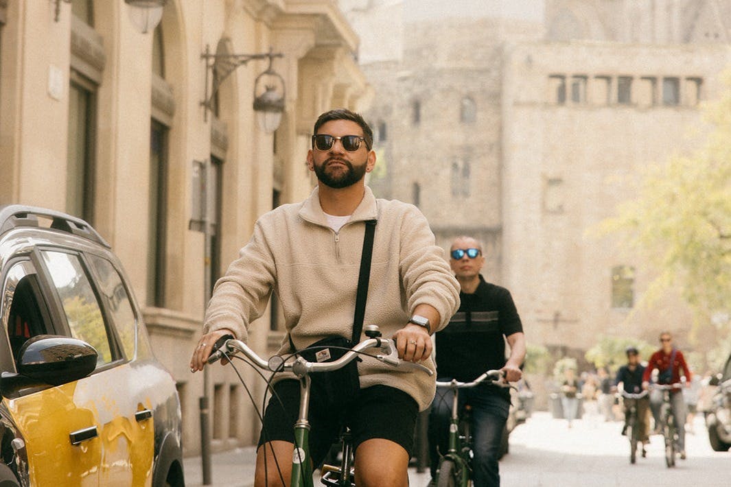Deux personnes circulant à vélo dans une rue avec des bâtiments historiques en arrière-plan par une journée ensoleillée.
