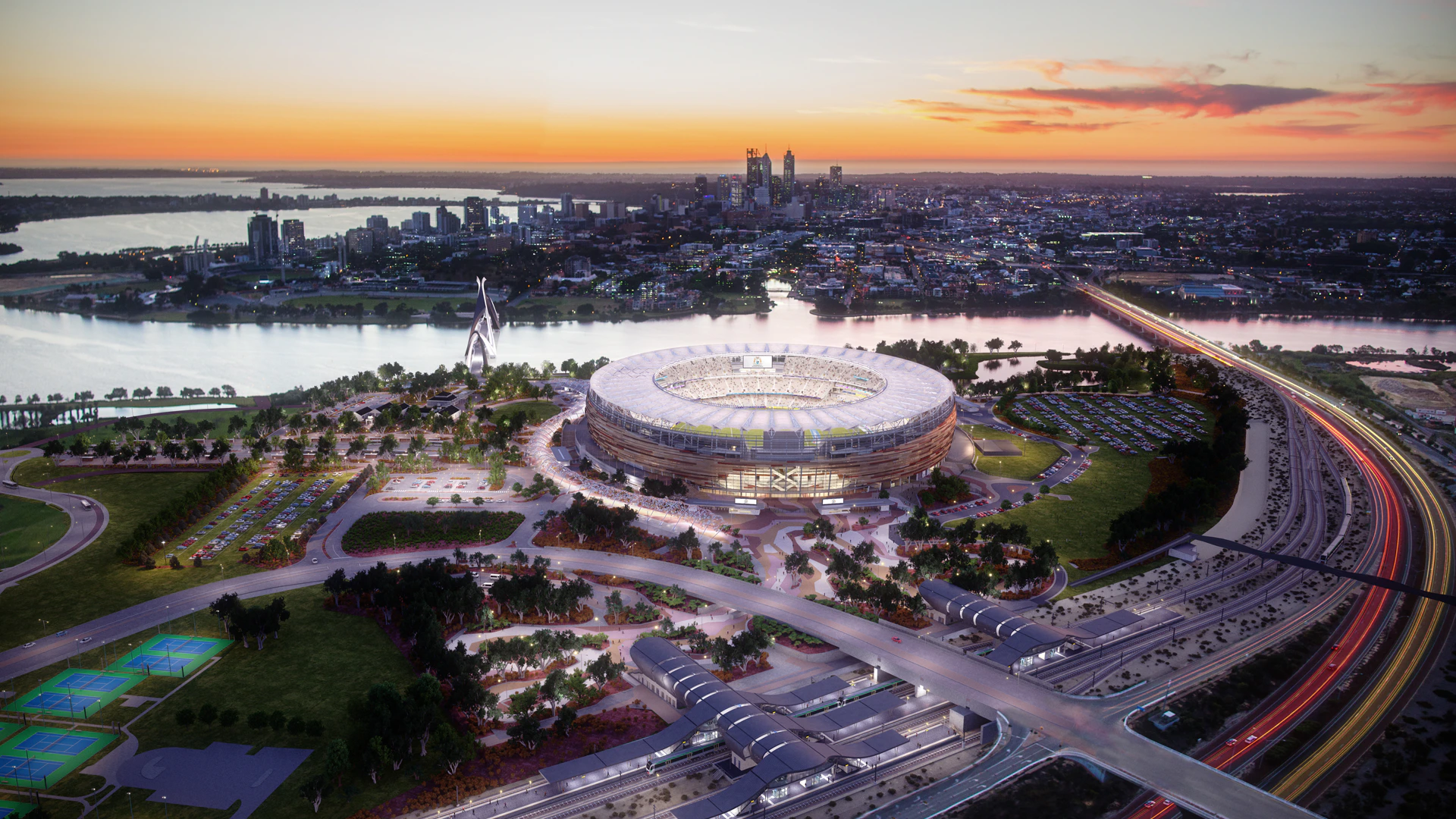 Aerial view of a large illuminated stadium near a river with a cityscape in the background at sunset.