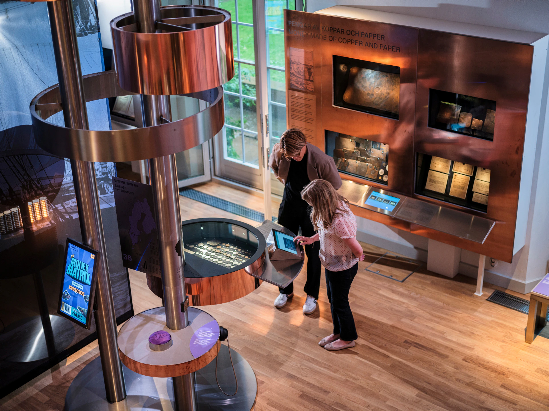 Two individuals examining exhibits in a modern museum featuring interactive displays and metallic structures.
