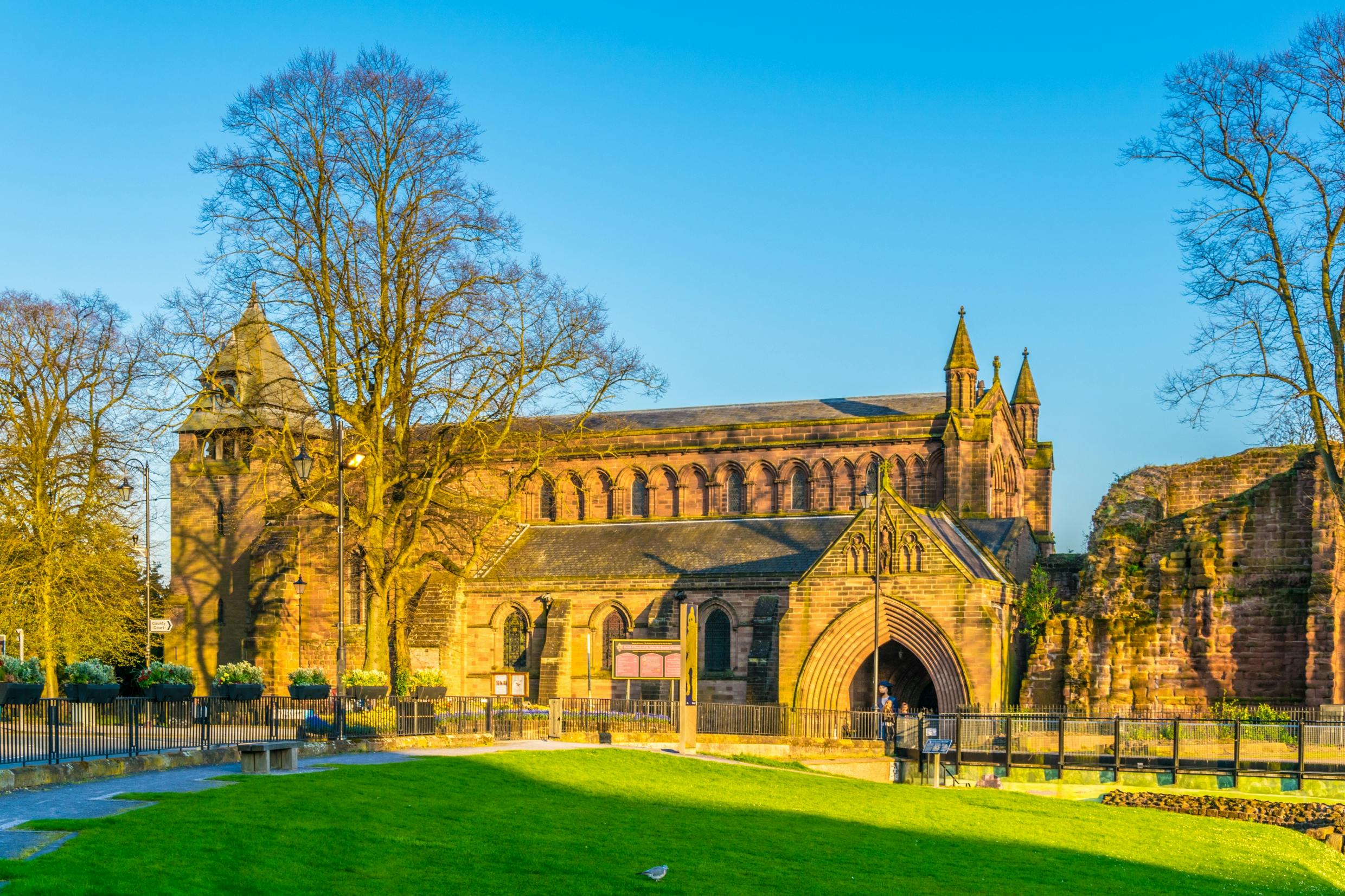 这座历史悠久的石头建筑设有拱形入口、大窗户和塔楼，坐落在晴朗的蓝天下，周围是一片草地。