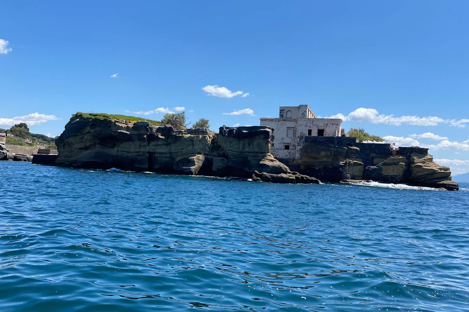 White building on a rocky shoreline against a clear blue sky and vibrant blue ocean water.
