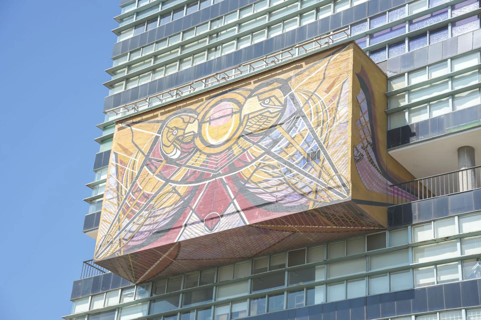 A colorful mural featuring abstract birds and geometric patterns on the façade of a modern building.