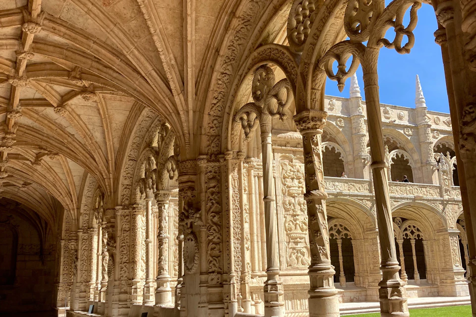 Ornately carved stone arches and columns of a historical building under a bright blue sky.