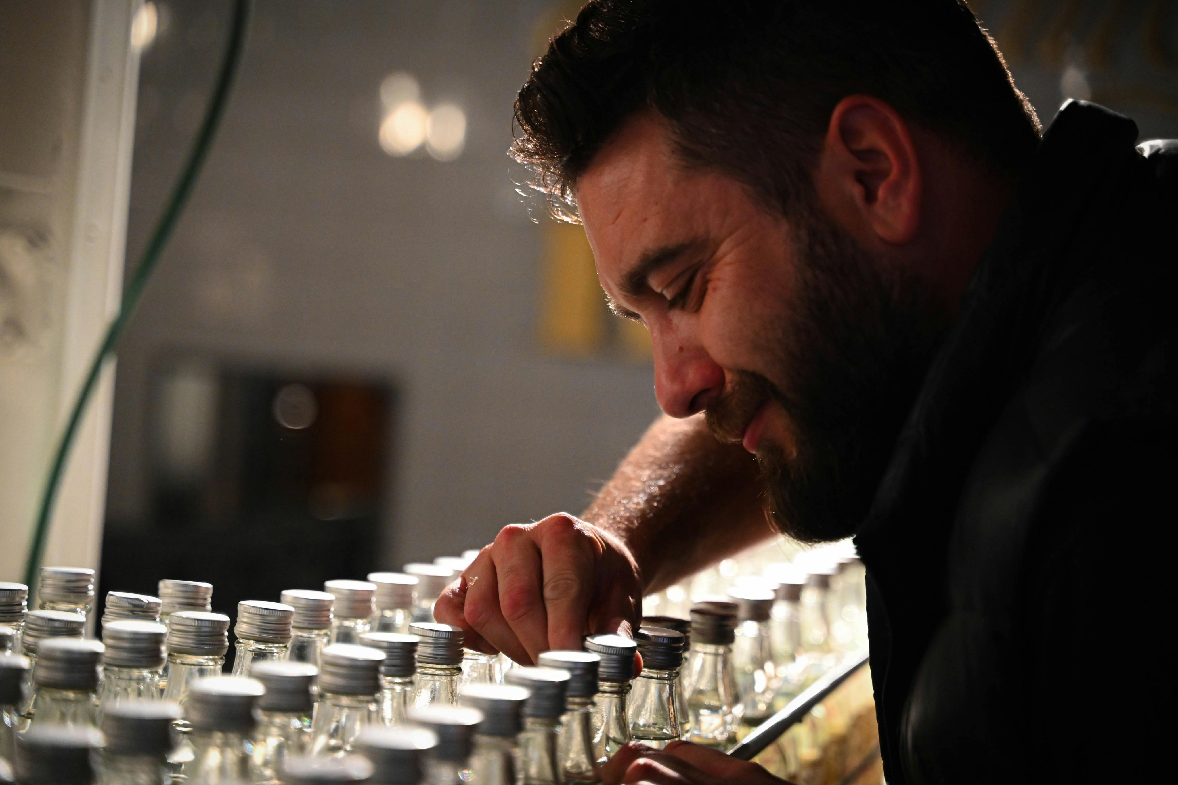 수염을 기른 남성이 뚜껑 옆에서 병을 들고 있다.