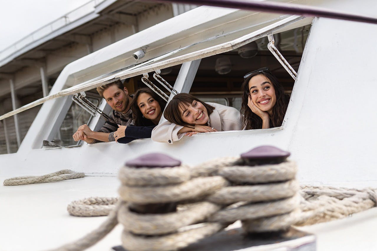 三名妇女在船上微笑着从窗户俯身而出，前景中可以看到绳索和船体结构的一部分。