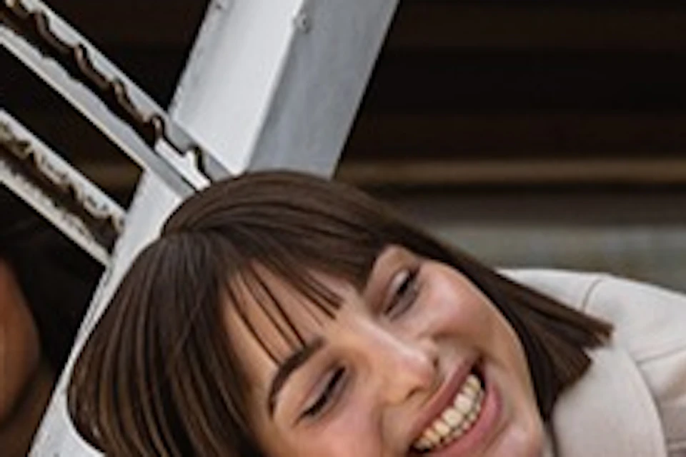 Three women smiling and leaning out of a window on a boat, with ropes and part of the boat's structure visible in the foreground.