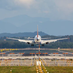Ett flygplan sedd bakifrån som lyfter från en landningsbana med berg och skog i bakgrunden.