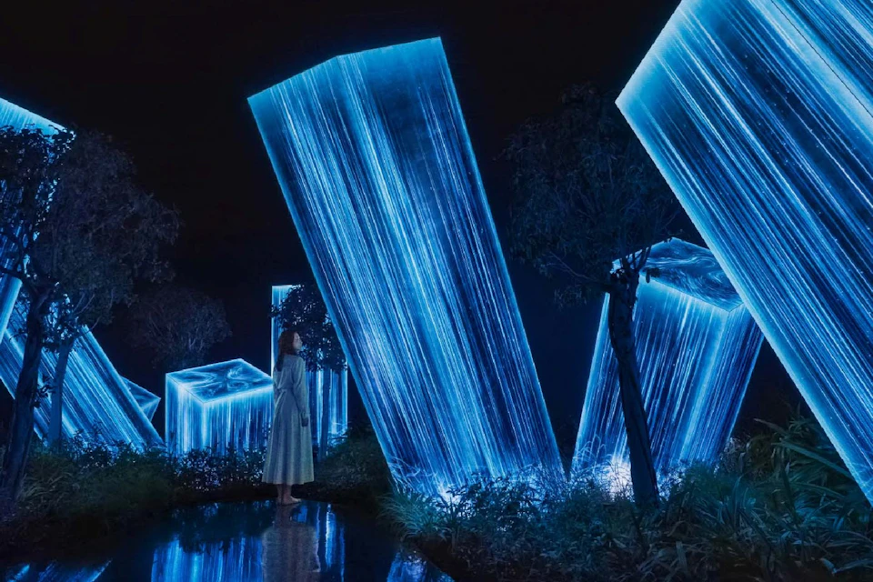A woman stands in a dark environment surrounded by glowing blue crystalline structures and trees.