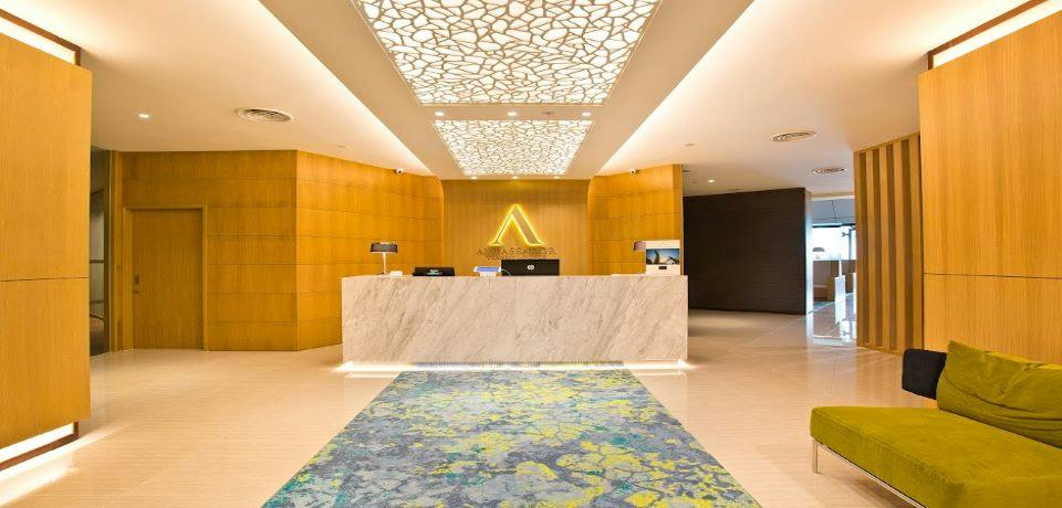 A modern reception desk in a well-lit lobby with a decorative ceiling and a patterned carpet in front.