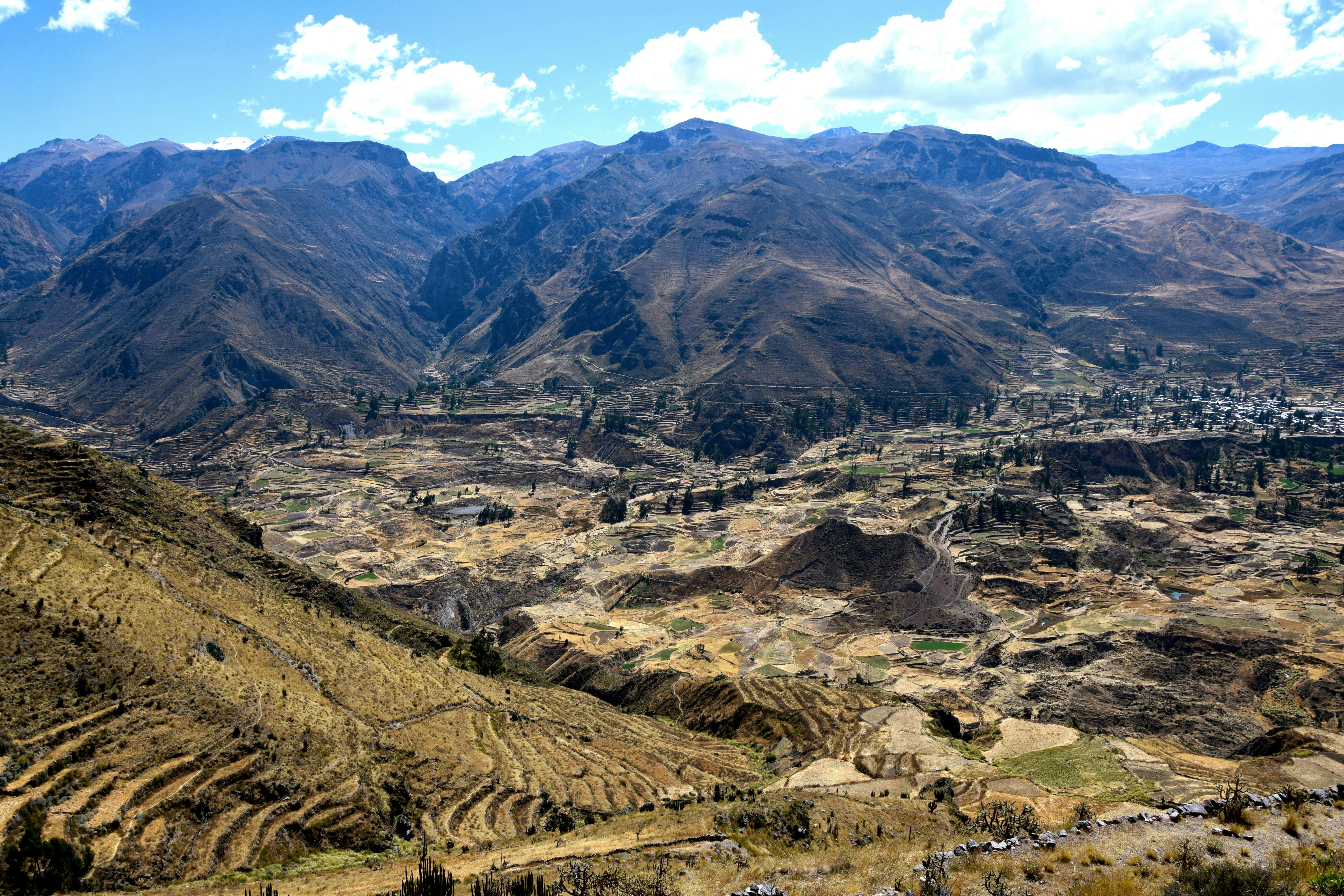 Долина с террасными полями и горами под частично облачным голубым небом.