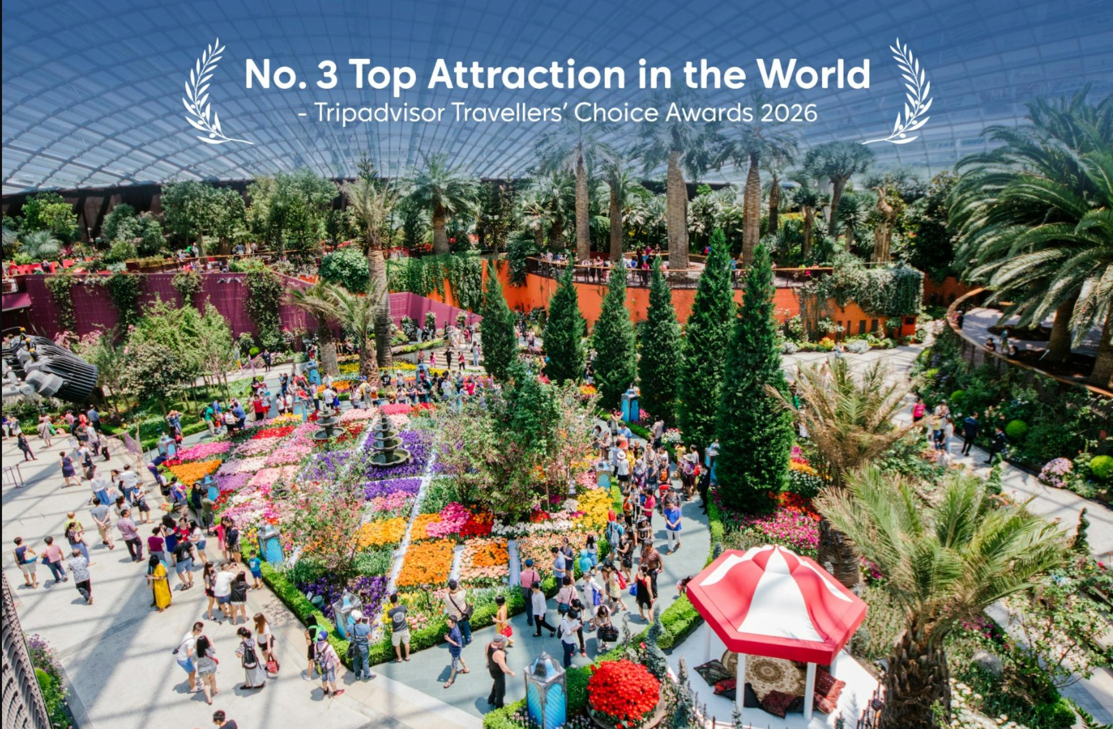En levande trädgård med färgglada rabatter, höga träd, besökare som går och text som nämner trädgårdens pris.