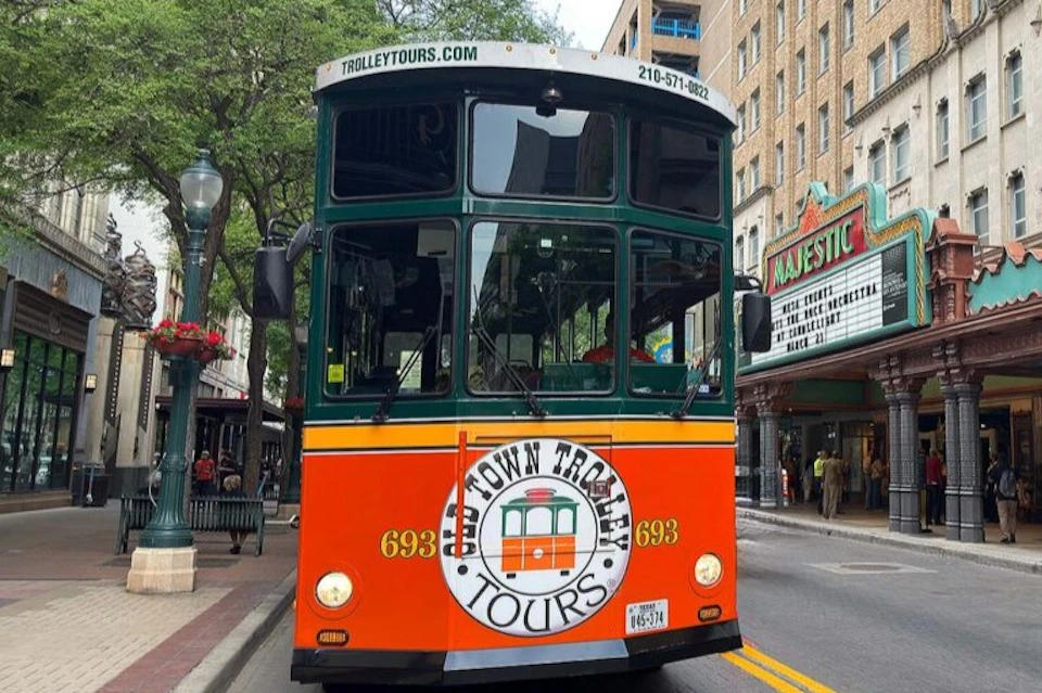 A bright orange and green trolley bus on a city street with a sign for "Old Town Trolley Tours" prominently displayed.