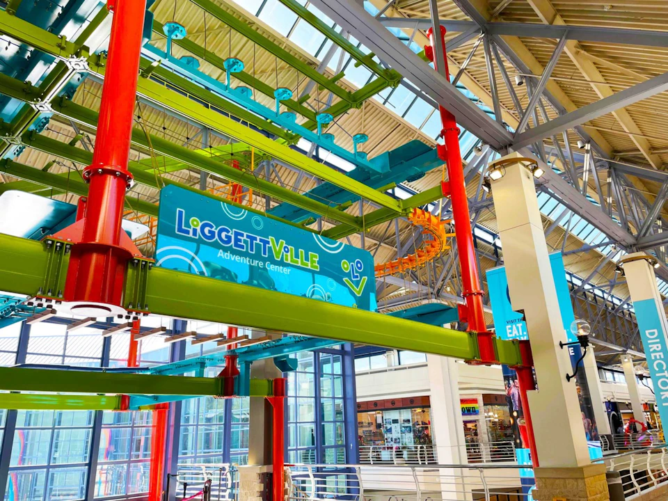 Indoor adventure center with colorful rope courses, featuring green, red, and blue structures, and a "LiGGEtTViLLE Adventure Center" sign.