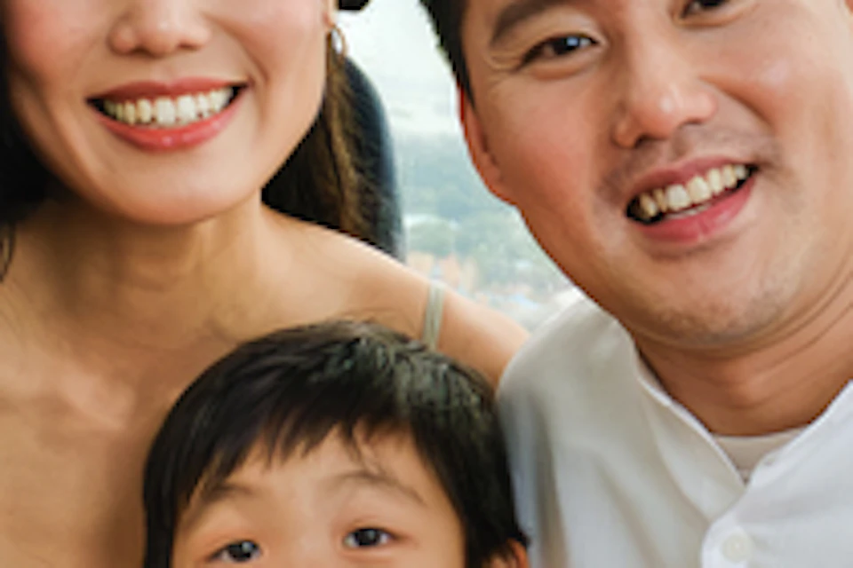 A family of three smiling inside a themed cable car cabin with cartoon decorations. A cable car is visible in the background.
