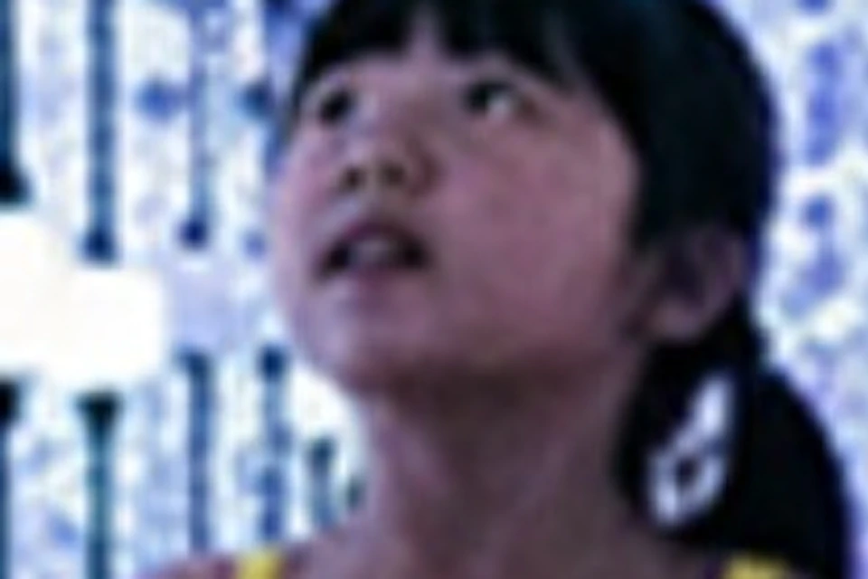 Two children stand among hanging strings of glowing orbs in a colorful, illuminated art installation.