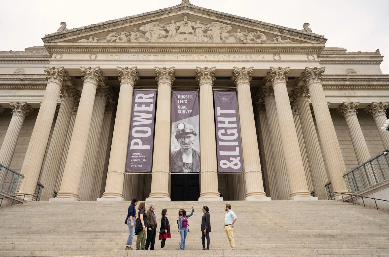 六个人站在美国国家档案馆大楼前的台阶上，横幅上写着“权力”和“光明”。