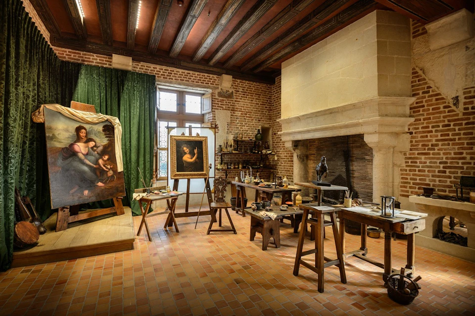 A recreated artist's studio with paintings, easels, a fireplace, wooden furniture, and art supplies on display.