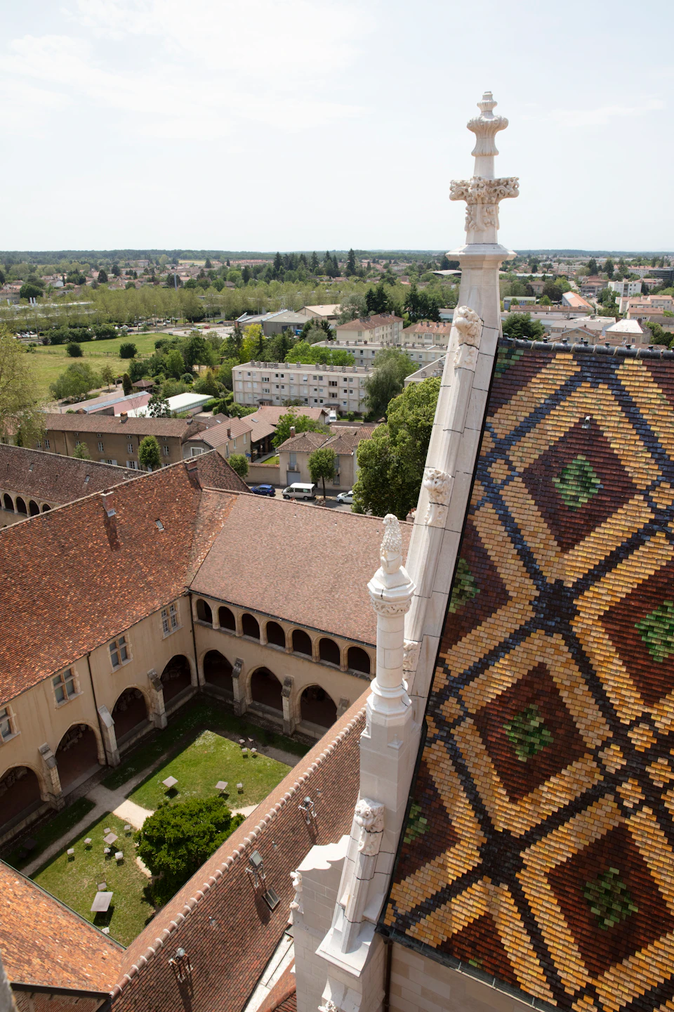 Colorful tiled roof of a historic building, overlooking a peaceful courtyard with arches, and a town with greenery in the background.