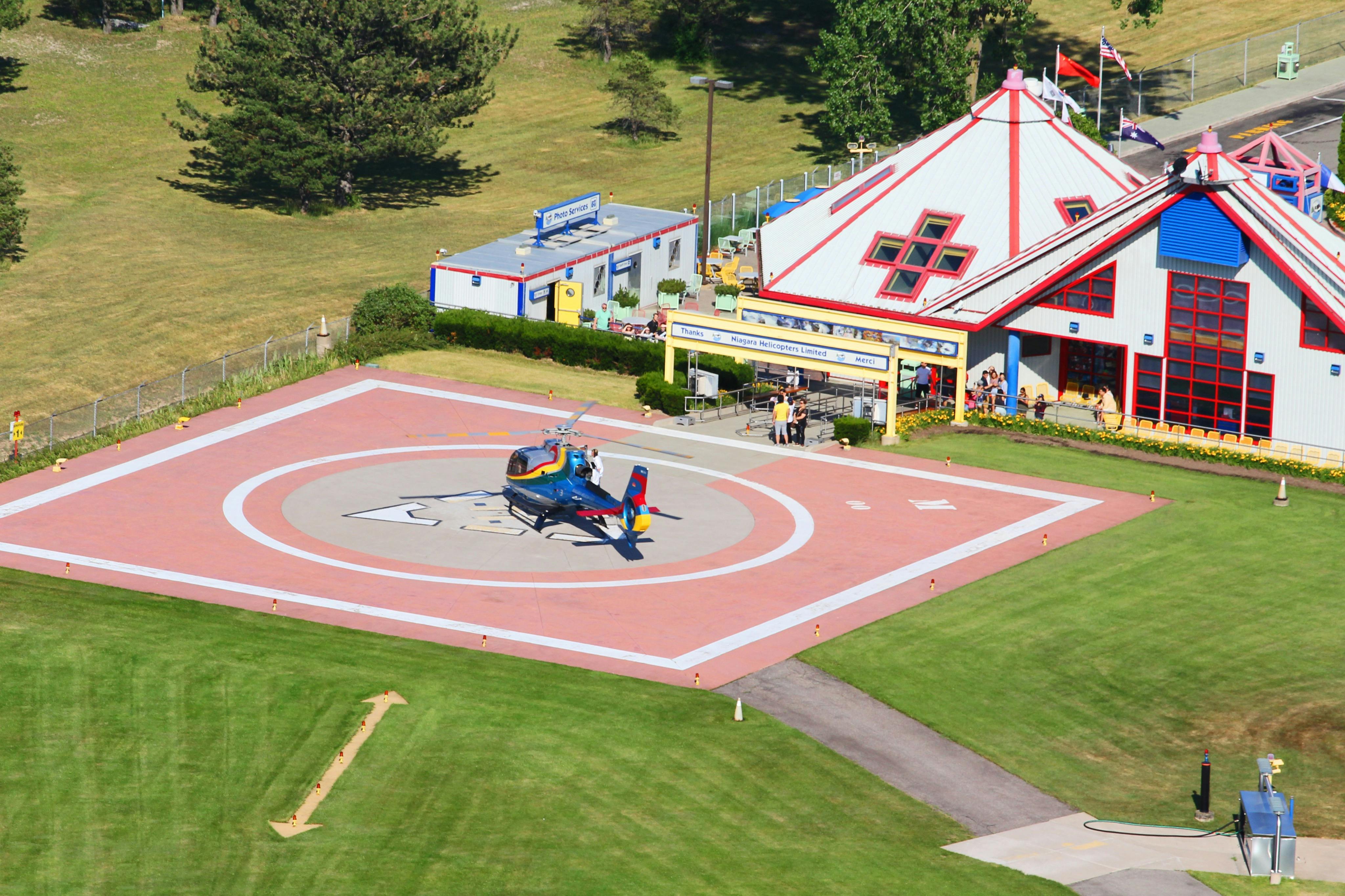 A helicopter on a helipad next to a building with a red roof, surrounded by green lawns and other smaller structures.