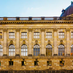 En historisk byggnad med välvda och rektangulära fönster, dekorativt stenverk och delvis utsikt över ett välvt tak.