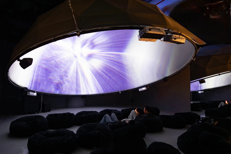 A large dome screen displaying a colorful abstract pattern, with people seated on bean bags underneath.
