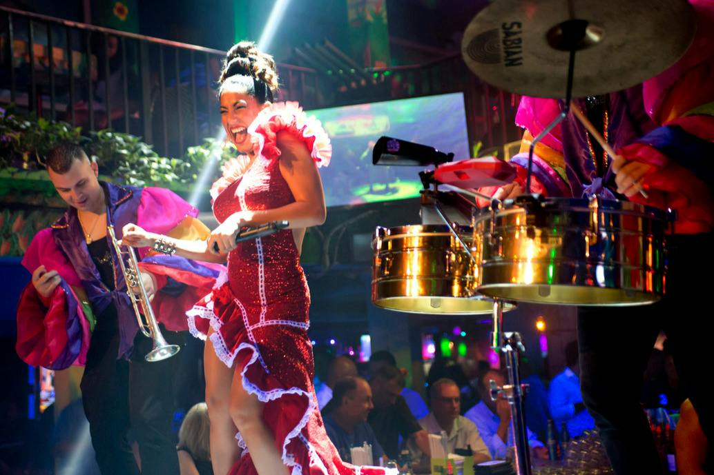 A lively performance with a woman in a red dress dancing and a man holding a trumpet on a vibrant stage with a crowd.