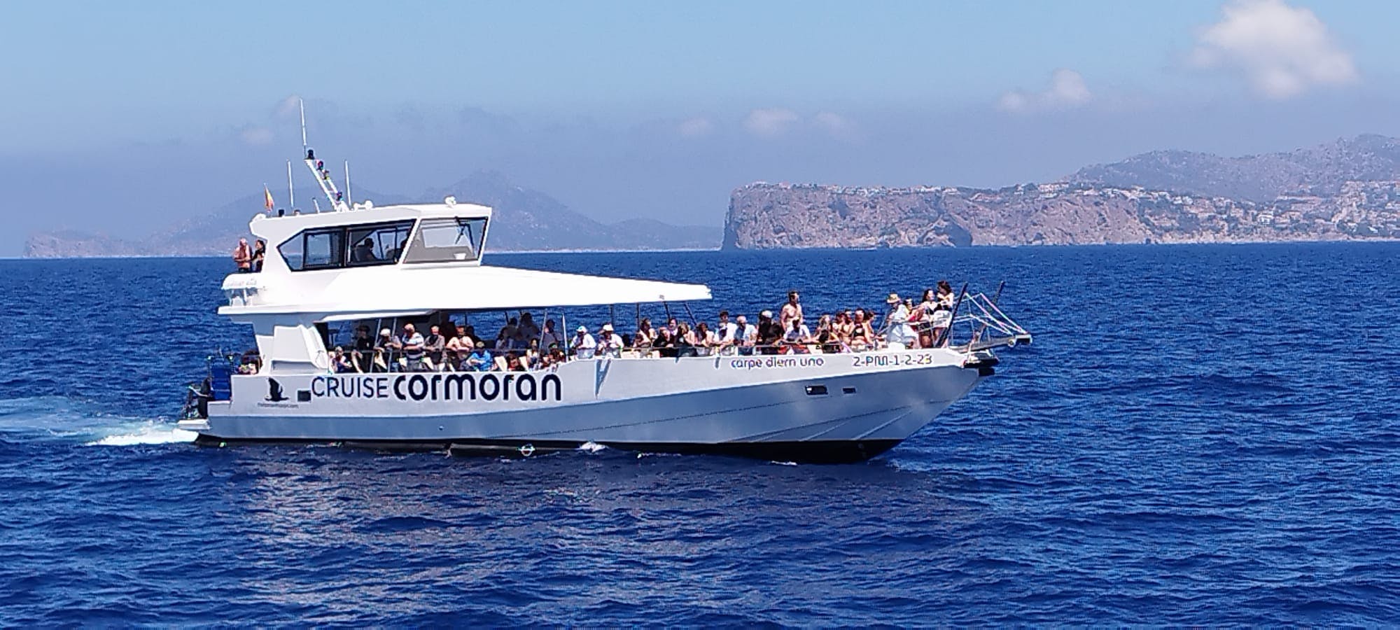 Un'imbarcazione chiamata "Carpe Diem Uno" che trasporta un gruppo di persone su acque blu e tranquille, con un'isola rocciosa visibile sullo sfondo.