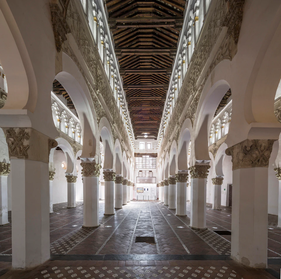 Ornate, arched interior with tall columns, decorative motifs, and a wooden ceiling. The room is spacious and well-lit.
