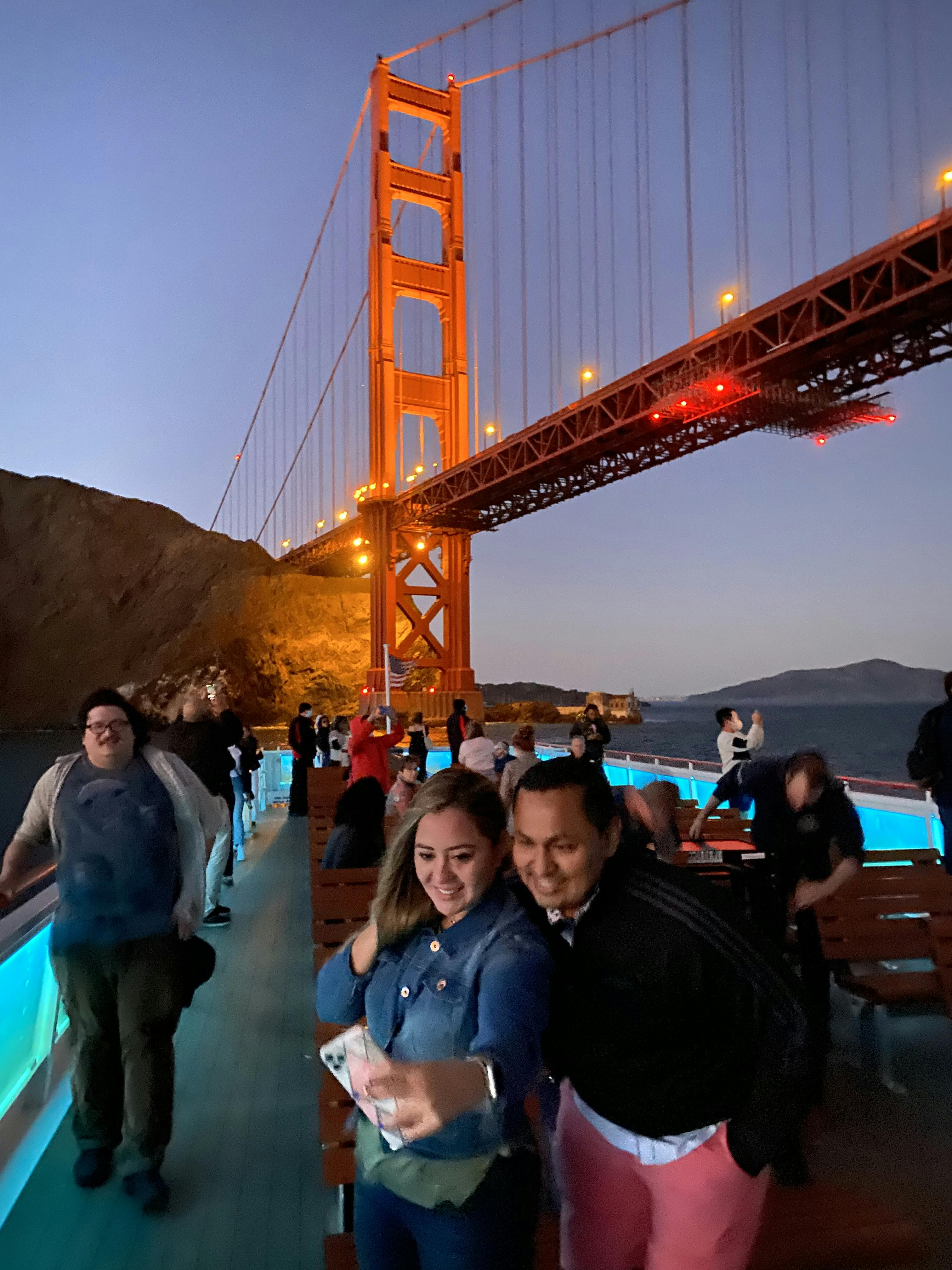 从船甲板上可以看到充满活力的水上日落，背景是一座桥梁和遥远的山丘。